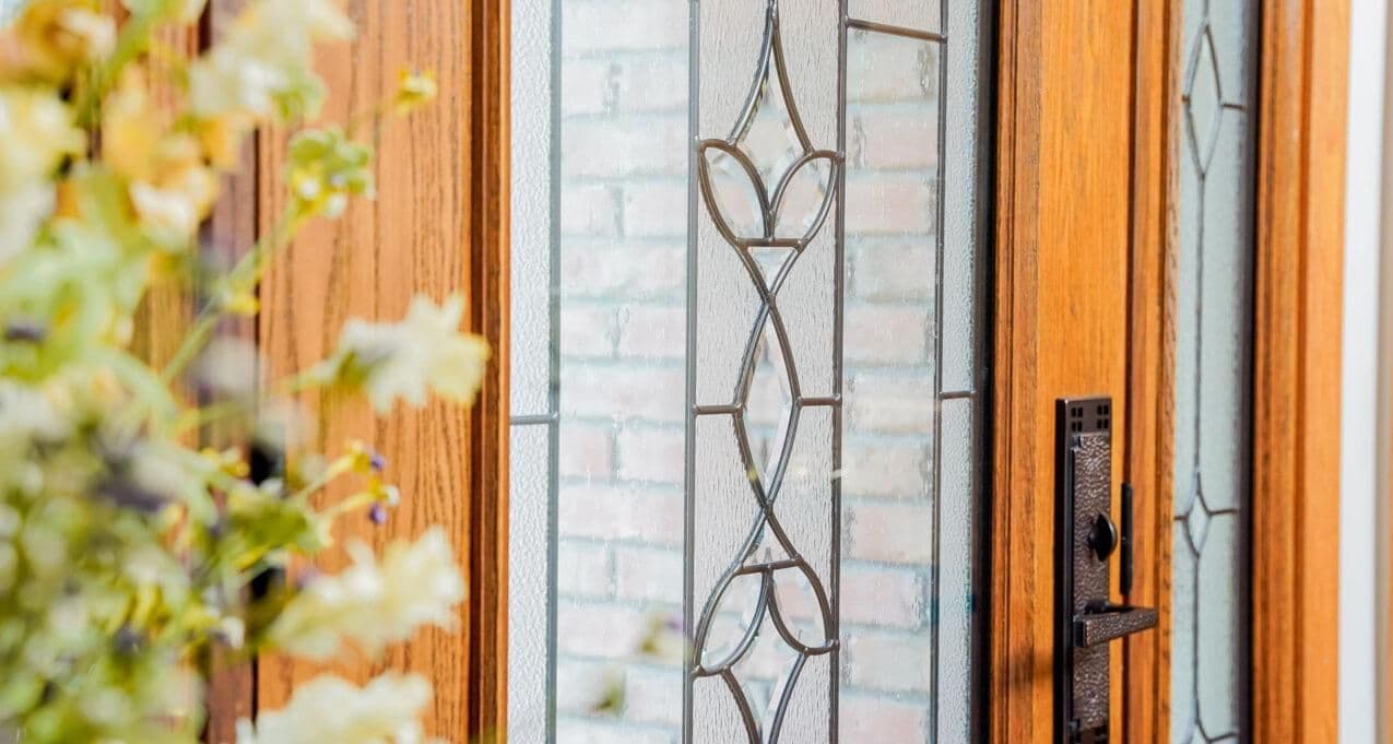 Close-up of wooden door with decorative stained glass and black handle, featuring flowers in the foreground