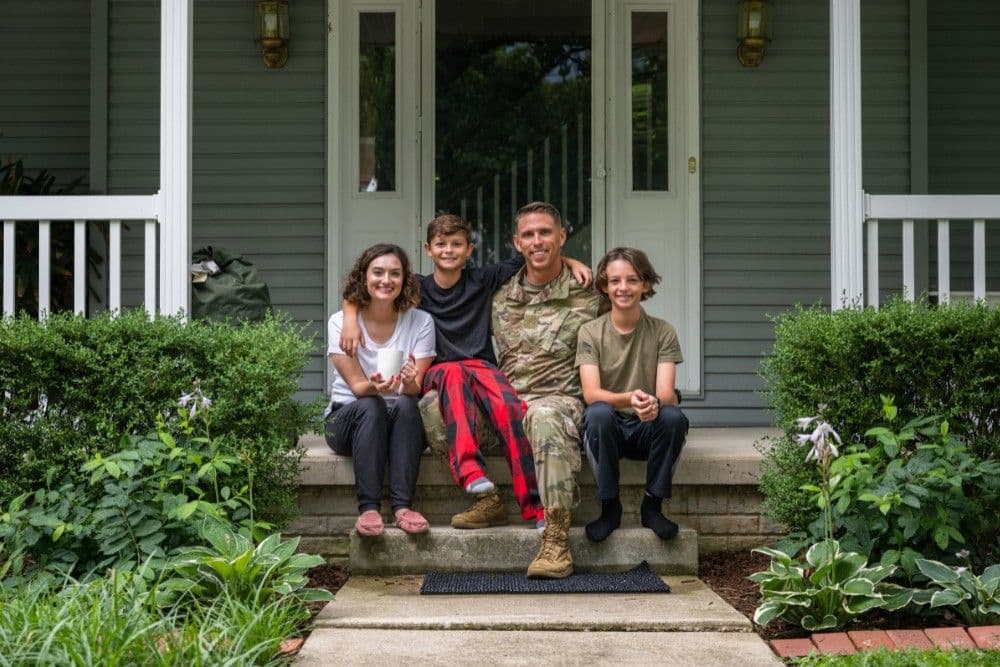 Family sitting on front porch steps of home with entry doors