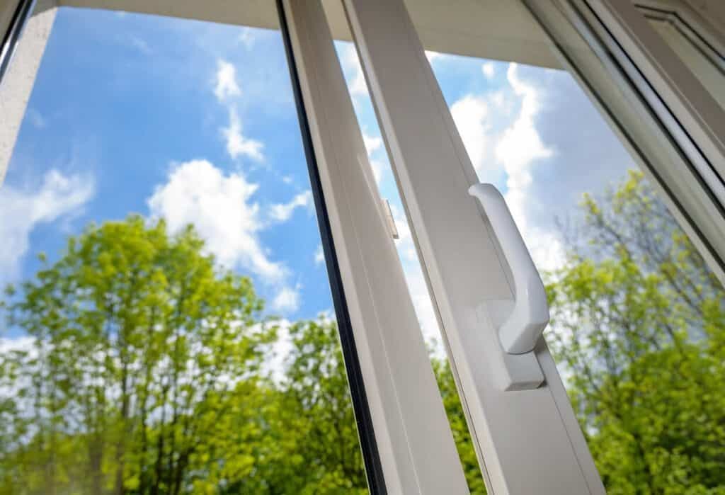 a white window with a handle and a view of trees.