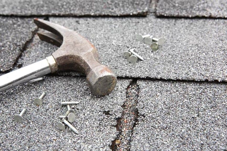 Weathered hammer on cracked asphalt shingle roof with scattered nails
